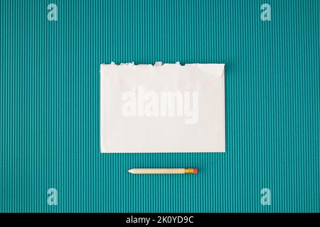 Busta bianca strappata e matita su sfondo blu. Concetto minimo con spazio di copia. Foto Stock