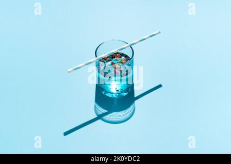 Bere in bicchiere blu con rose secche, peperoni rossi e paglia di carta a righe su sfondo blu. Foto Stock