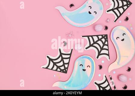 Grazioso piatto di Halloween colorato pastello con piatti a forma di fantasma, tovaglioli ragno e coriandoli su sfondo rosa Foto Stock