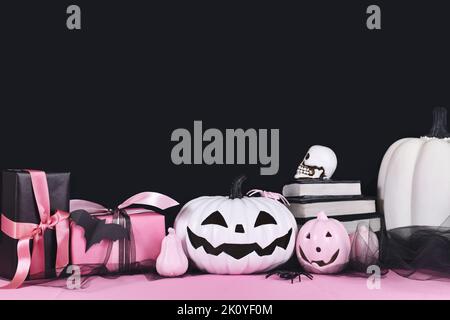 Decorazioni di Halloween rosa e bianco con zucche bianche e nere, libri di magia e ragni su sfondo nero con spazio copia Foto Stock