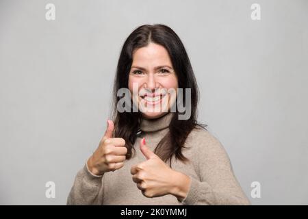 ritratto di una donna che mostra un gesto di pollice-su con entrambe le mani Foto Stock
