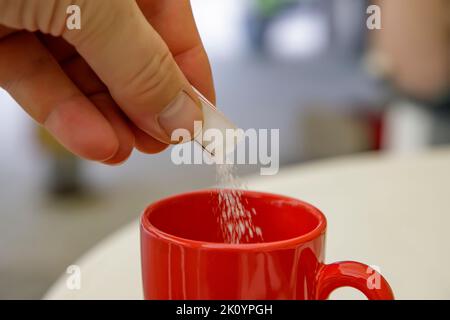 mettere lo zucchero a mano in una tazza di caffè o tè. Chiudi Foto Stock