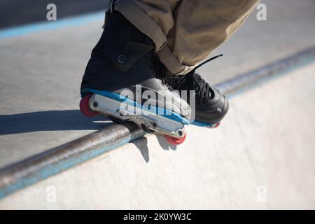 Roller blader smerigliatura su rotaia in skatepark. Skater in linea che esegue il trucco BS Unity Grind in mini rampa all'aperto Foto Stock