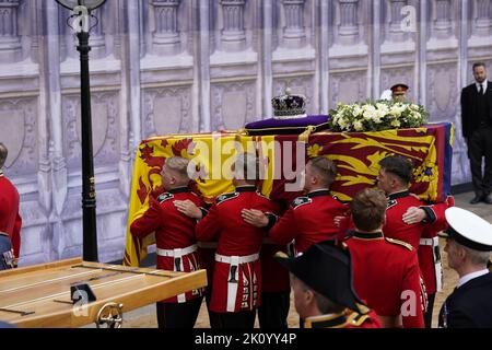 Il partito portatore trasporta la bara, drappeggiato nello Standard reale con la corona di Stato imperiale posta in cima, della regina Elisabetta II, nella sala di Westminster, Londra, dove si trova in stato davanti al suo funerale il lunedì. Data immagine: Mercoledì 14 settembre 2022. Foto Stock