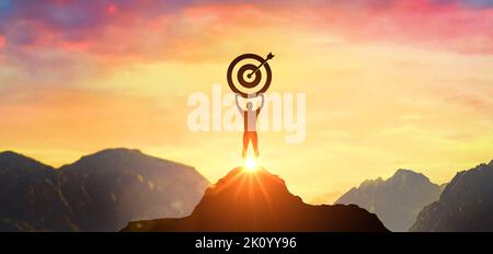Raggiungere con successo il vostro obiettivo. Leadership aziendale di successo, vincitore in testa. Silhouette uomo d'affari che tiene il bersaglio in cima alla montagna, cielo e luce solare Foto Stock