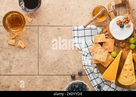 Assortimento di formaggi, miele, cracker, mirtilli, uva con vino rosso e bianco in bicchieri antipasto server su tavola di marmo bianco su fondo grigio Foto Stock