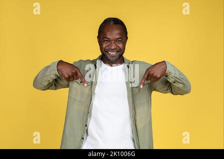 Felice uomo africano americano maturo felice in casual mostrando le dita giù su spazio vuoto, guardare la macchina fotografica Foto Stock
