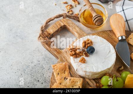 Assortimento di formaggi, miele, cracker, mirtilli, uva con vino rosso e bianco in bicchieri antipasto server su tavola di marmo bianco su fondo grigio Foto Stock