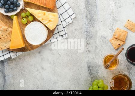 Assortimento di formaggi, miele, cracker, mirtilli, uva con vino rosso e bianco in bicchieri antipasto server su tavola di marmo bianco su fondo grigio Foto Stock