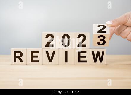 2023 revisione del nuovo anno. L'uomo d'affari gira il cubo di legno e cambia le parole dalla revisione 2022 alla revisione 2023. Business, 2023 revisione del concetto di nuovo anno. Capovolgimento di Foto Stock