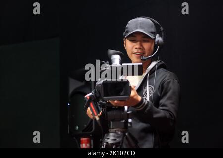 Cameraman con una fotocamera su un cavalletto in studio Foto Stock