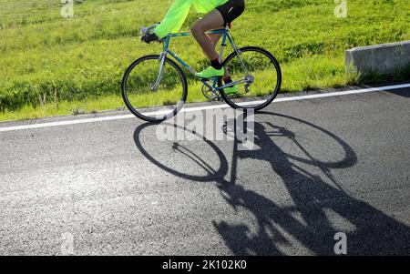 il ciclista corre veloce contro la luce con una storica bici da corsa sulla strada asfaltata Foto Stock