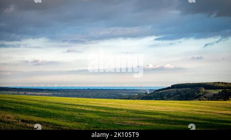 Una vista attraverso i campi e verso una fattoria eolica offshore nel tardo pomeriggio nel South Downs National Park, West Sussex, Regno Unito Foto Stock