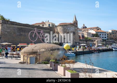 Statua rosa delle biciclette da corsa con vista sulla cittadella del centro storico e sul porto dal porto di Alghero, Sardegna, Italia Foto Stock