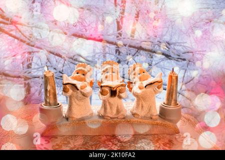 Decorazione di tre angeli in gesso con candele che cantano le lodi per Natale sullo sfondo di un paesaggio invernale. Un biglietto d'auguri. Foto Stock