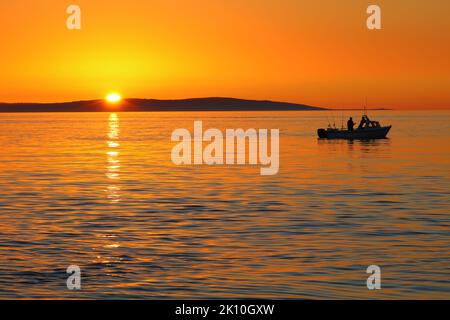 Splendido tramonto arancione con silhouette di piccola barca e Isola di Anglesey sullo sfondo. Anglesey, Galles del Nord, Regno Unito. Foto Stock