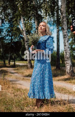 Una giovane bella donna in un abito blu tiene i fiori selvatici nelle sue mani Foto Stock