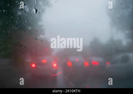 Retroilluminazione rossa delle auto. Immagine ripresa attraverso gocce di pioggia che cadono su vetro bagnato, sfocature astratte del traffico - monsone stock immagine di Kolkata (ex Calcut Foto Stock