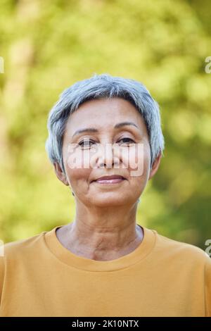 Headshot ritratto piuttosto anziano grigio capelli pensionato donna con taglio corto sorridente guardare la macchina fotografica posa all'aperto da solo sul parco estivo alberi verdi sunn Foto Stock
