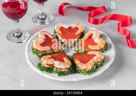 Canape in forma di cuori con caviale rosso e gamberi su piatto bianco su sfondo grigio chiaro, festa di San Valentino Foto Stock