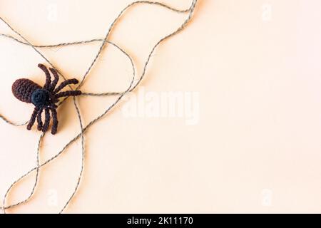 Concetto di Halloween. Ragno nero lavorato a maglia e rete beige da fili su uno sfondo arancione con spazio per il testo, piatto Foto Stock