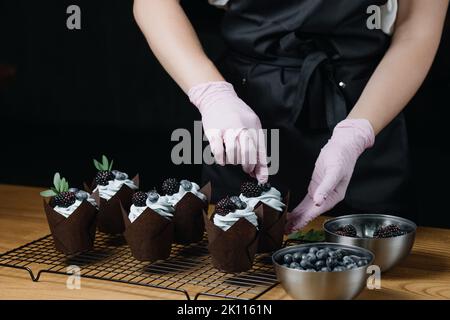 Cupcake al cioccolato con crema mista. Le mani femminili riempiono i cupcakes con le bacche fresche. Foto Stock