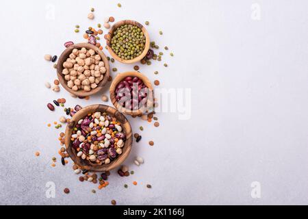 Vista dall'alto di diversi fagioli, lenticchie, mung, ceci in ciotole di legno per gustosi pasti su sfondo grigio cemento con spazio copia Foto Stock