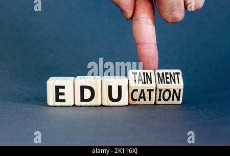 Simbolo dell'istruzione e dell'edutainment. Concetto di parole Educazione ed edutainment su cubi di legno. Mano dell'insegnante. Bellissimo sfondo grigio tavolo. Educati Foto Stock