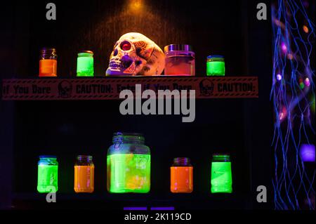 Un cranio, nastro di attenzione e vasi con liquido verde e arancione al neon sullo scaffale di un fresco, indoor Halloween party. Idee alternative di decorazione dell'anca. Foto Stock