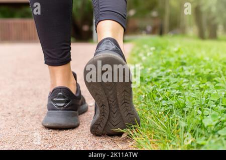 gambe di donna, in sneaker nere , camminando lungo un sentiero fatto di piccola pietra rossa Foto Stock