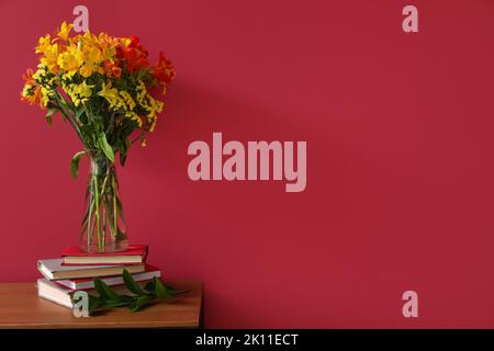 Pila di libri e vaso con fiori di alstroemeria sul tavolo vicino alla parete colorata Foto Stock