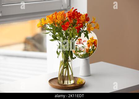 Vaso con bellissimi fiori di alstroemeria e specchio vicino alla finestra Foto Stock