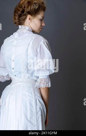 Donna edoardiana che indossa una blusa in pizzo bianco e una gonna sullo sfondo grigio di uno studio Foto Stock