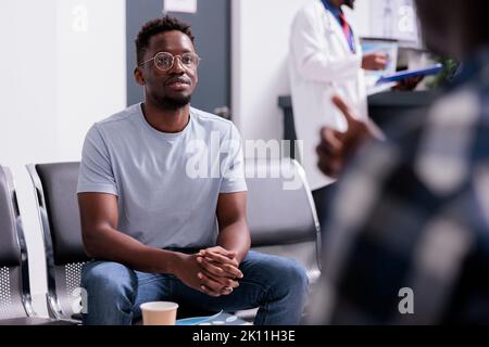 Pazienti afroamericani che parlano di assistenza sanitaria e diagnosi nella lobby della sala d'attesa presso il centro sanitario. Gruppo di uomini seduti nella zona della reception dell'ospedale prima di partecipare all'esame di controllo. Foto Stock