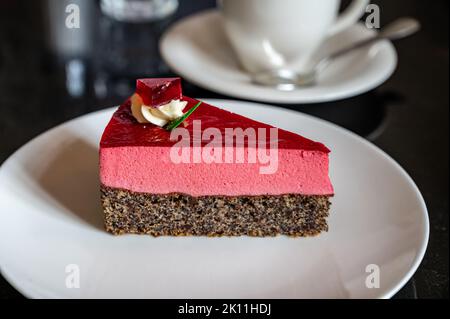 Pezzo di famosa torta di semi di papavero con mousse di lamponi di origine austriaca servito con panna montata e tazza di caffè in vecchio classico caffè-ristorante in Foto Stock