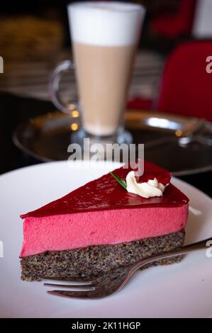 Pezzo di famosa torta di semi di papavero con mousse di lamponi di origine austriaca servito con panna montata e una tazza di caffè latte in vecchio classico caffè-ristorante Foto Stock