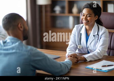 Donna sorridente afro-americana medico tenendo la mano paziente Foto Stock
