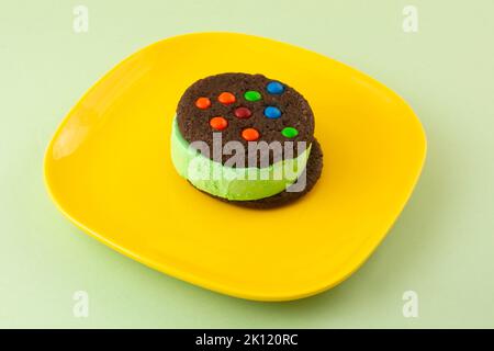 Sandwich con gelato alla menta con biscotti al cioccolato e caramelle su piatto da dessert giallo Foto Stock