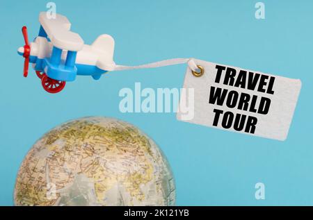 Concetto di viaggio e di affari. Su uno sfondo blu, un globo e un aereo con un cartello - Travel World tour. Globo fuori fuoco. Foto Stock