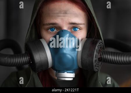 Sopravvivenza femminile post-apocalisse. Giovane donna sopravvissuta pandemica in maschera a gas che guarda di fronte a lei sullo sfondo con area di guerra apocalittica arou Foto Stock