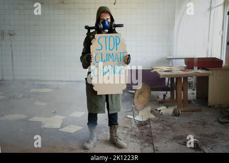 Survivor post-apocalittico femminile in maschera a gas con banner dice fermare il cambiamento climatico. Concetto di disastro Foto Stock