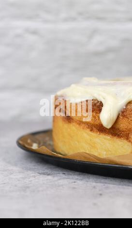 primo piano di crema di burro glassa sulla torta di cannella roll, sfondo bianco, tavolo in marmo grigio Foto Stock