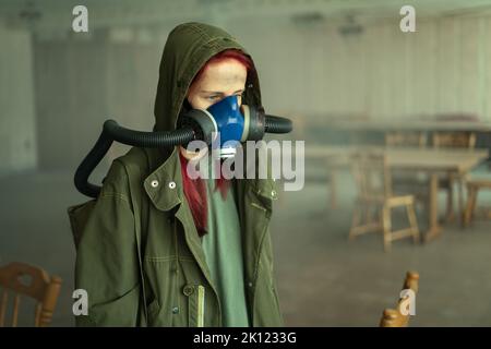 donna post-apocalittica, che vive in un edificio abbandonato indossando una maschera a gas sotto il cappuccio attutito Foto Stock