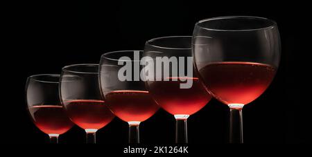 bicchieri con vino rosso su sfondo nero, lunga disposizione eleganti bevande alcoliche. Foto Stock