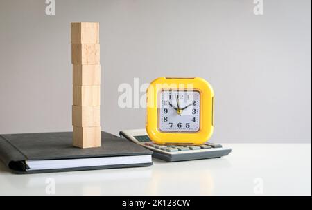 Sei cubetti di legno vuoti impilati su un blocco note con calcolatrice e orologio accanto ad esso. Testo libero e modello per concetto di business. Foto Stock