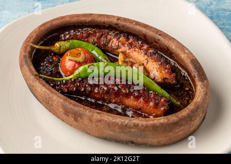 Polpo in casseruola con pomodori e peperoni su fondo di pietra blu Foto Stock