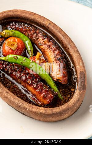 Polpo in casseruola con pomodori e peperoni su fondo di pietra blu Foto Stock