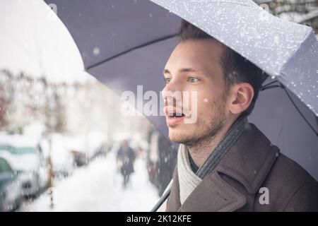 Ritratto di un bel giovane uomo con ombrello che respira aria calda nella neve d'inverno Foto Stock