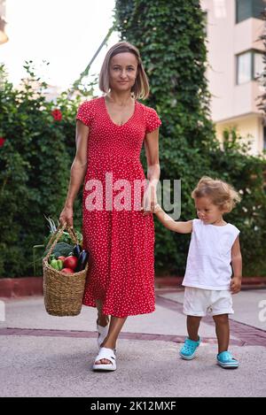 madre e suo figlio con un cesto di frutta e verdura dal mercato agricolo Foto Stock