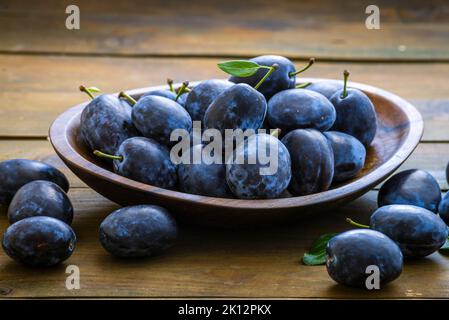 Blu maturo fresco prugne dolci organici appena raccolti dall'albero, piatto ciotola in legno di noce al coperto. Autunno raccolta di frutta rustico legno nero scuro ba Foto Stock